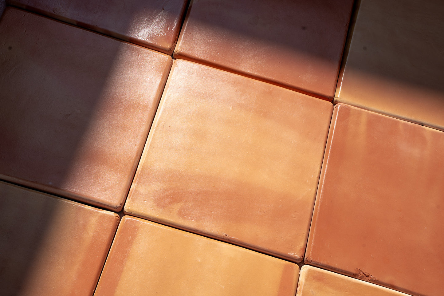 Rounded 16x16 terracotta tiles by Clay Imports in earthy reddish-orange tones, with textured surface and diagonal sunlit shadows.