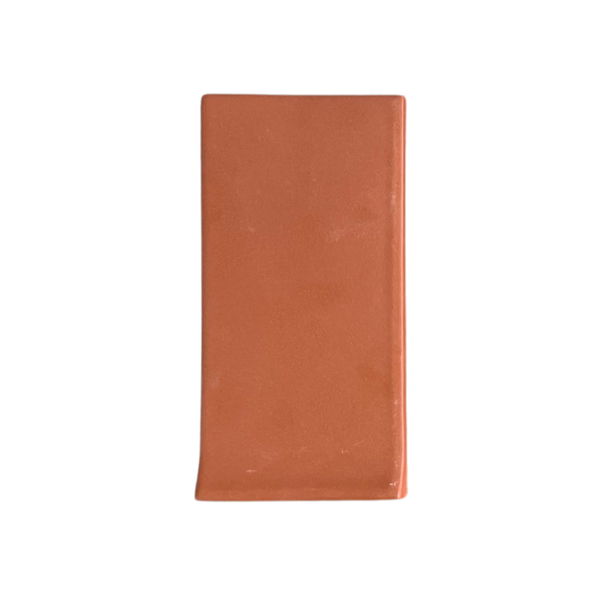A terracotta Bota Mamey rectangular tile by Clay Imports, with a smooth surface and one curved bottom edge.
