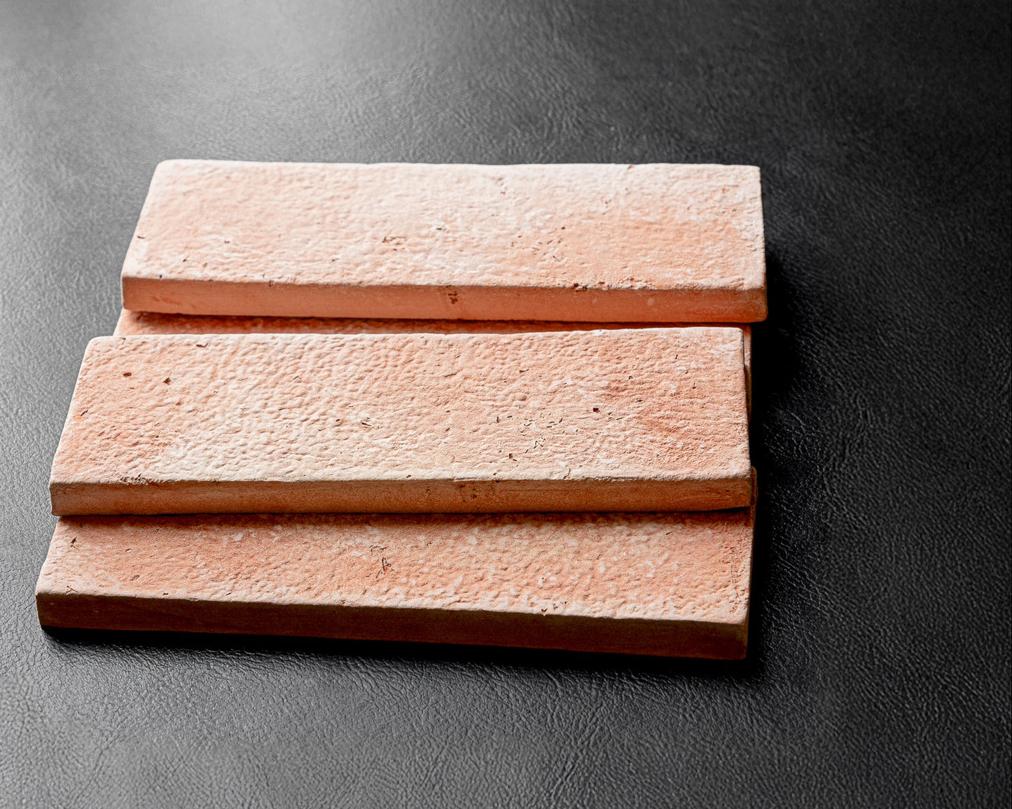 Three Umbria Matte Terracotta 2.5x8 tiles by Clay Imports, stacked on a dark textured surface.