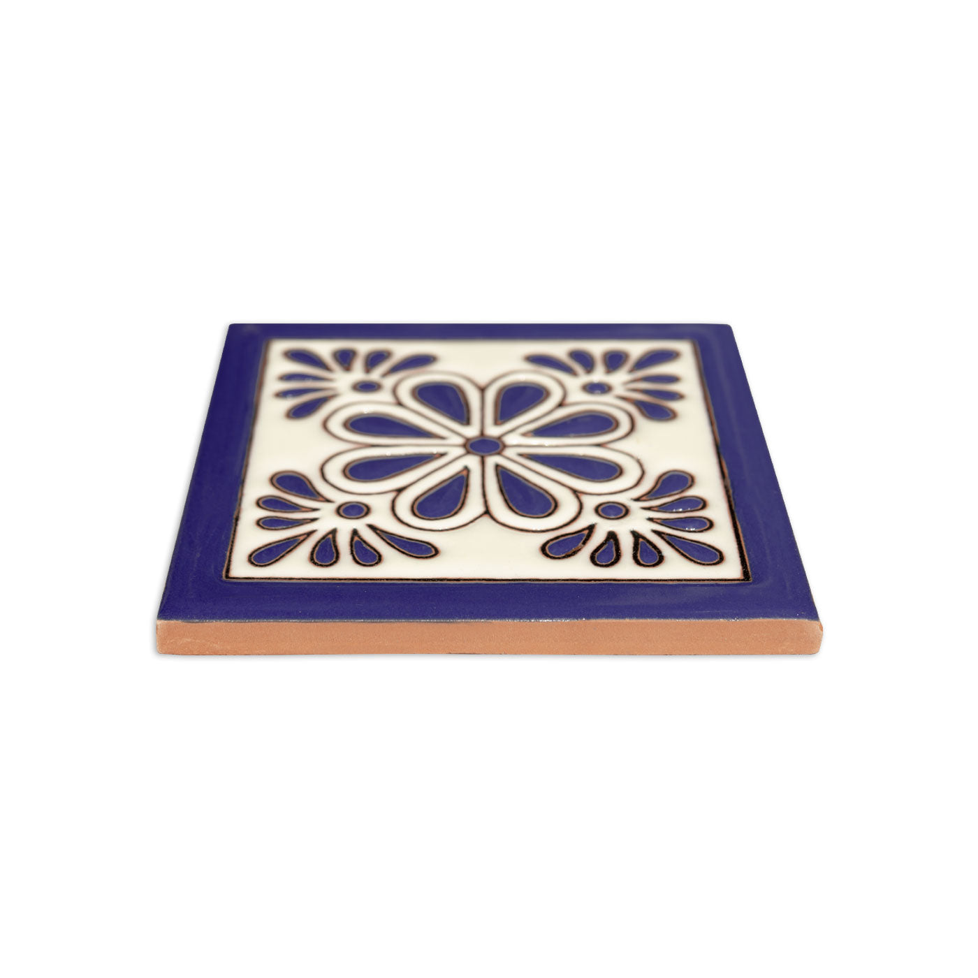 White and dark blue relief Talavera tile by Clay Imports with a central gerbera flower design, bordered in blue, showing a terra cotta edge.