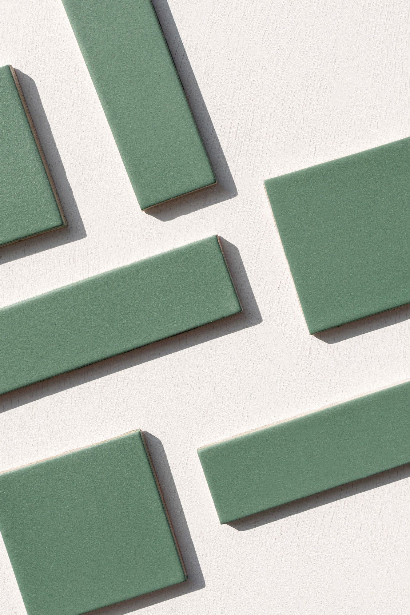 Cilantro green rectangular clay tiles by Clay Imports, arranged diagonally on a textured white surface.