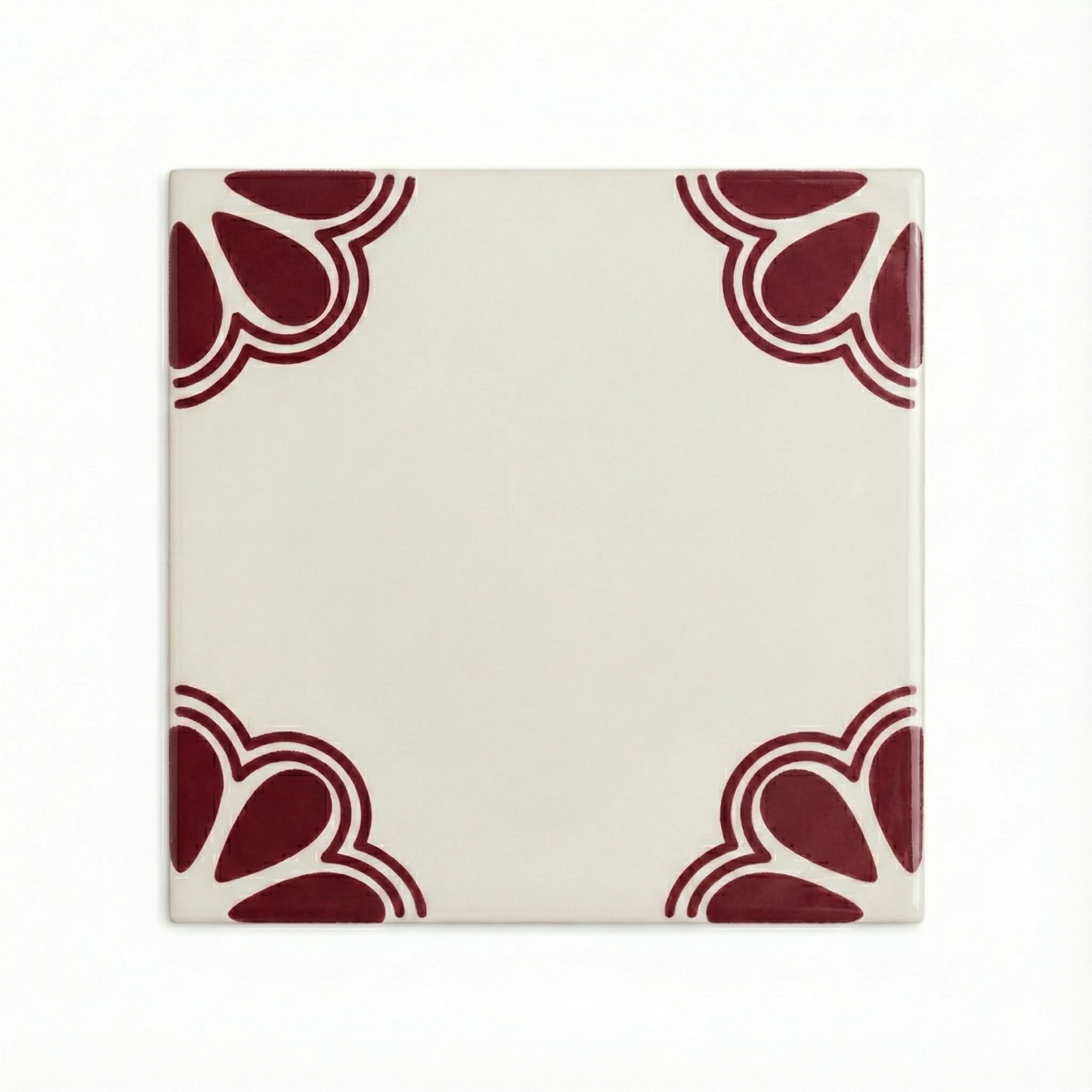 Oxblood and cream Talavera tile sample by Clay Imports Handmade Tile, featuring stylized dark red corner patterns on a glossy cream base.
