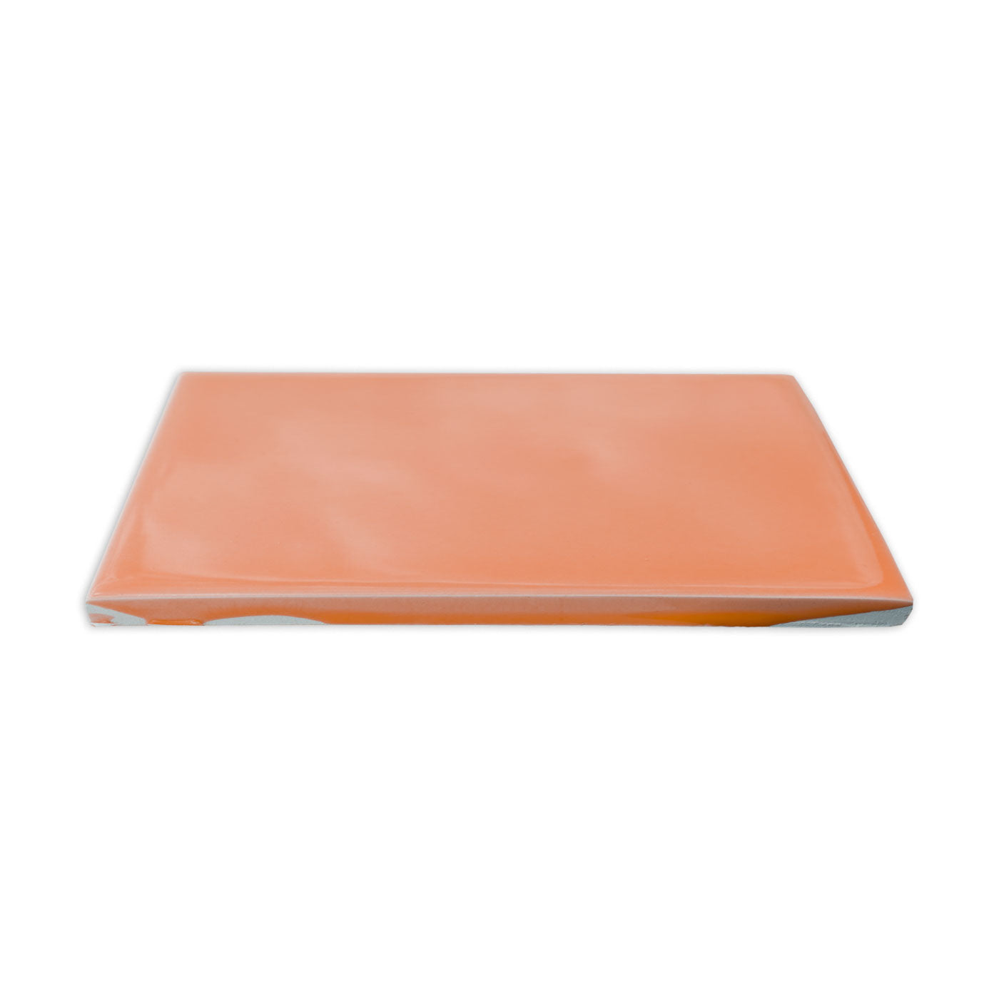 Glossy orange rectangular solid tile by Clay Imports, viewed from a slight side angle showing its light gray bottom edge.