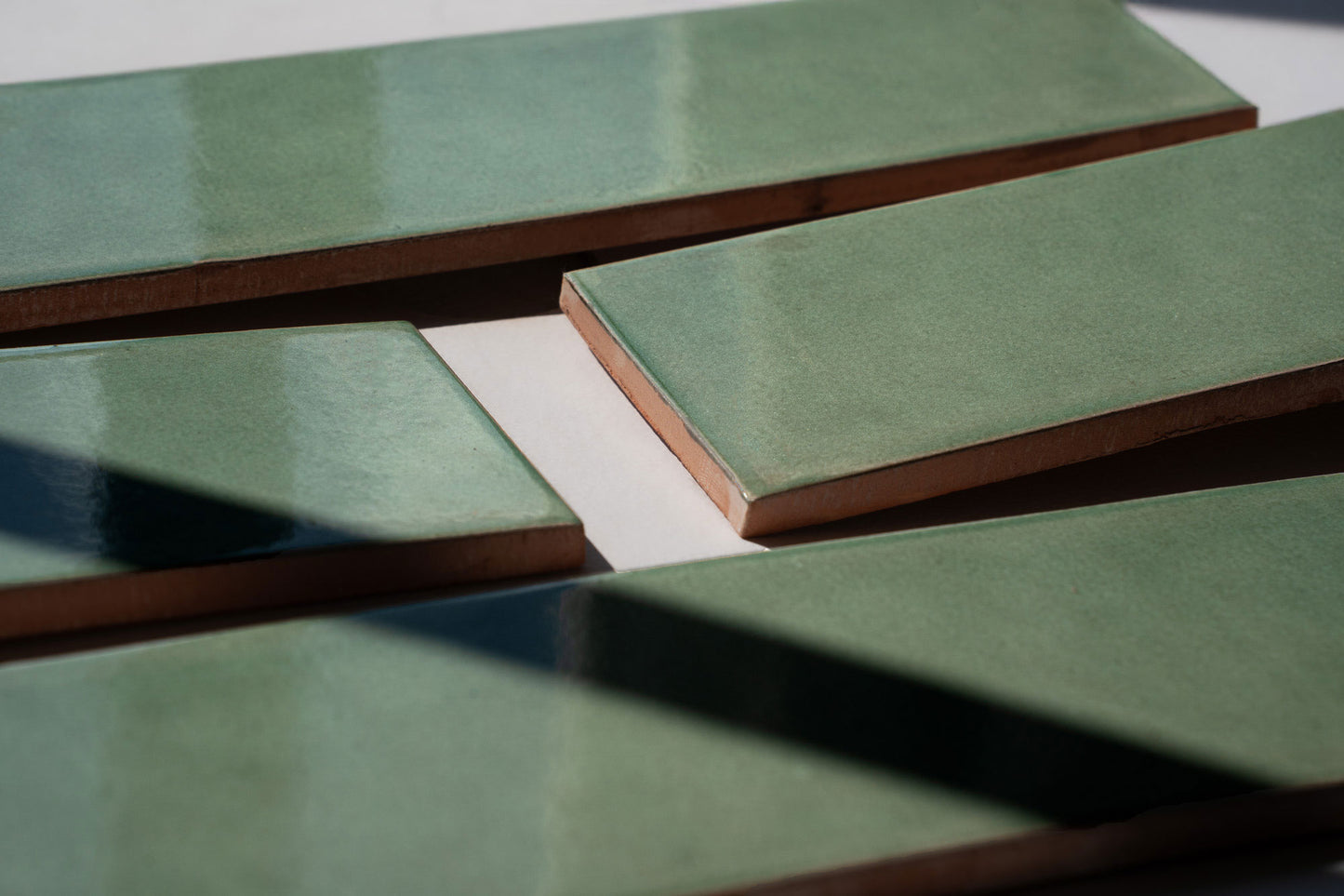 Sage green rectangular solid tile with matte finish and terracotta edge, arranged in overlapping display with natural shadow accents