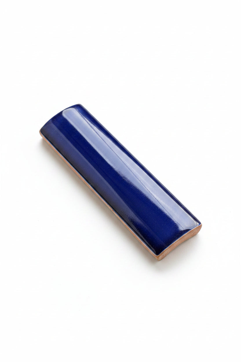 A glossy dark blue ceramic tile with a curved surface rests on a white background.