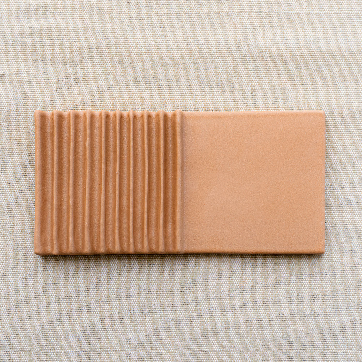 Terracotta clay tile by Clay Imports, half-ribbed and half-smooth, on light beige fabric.