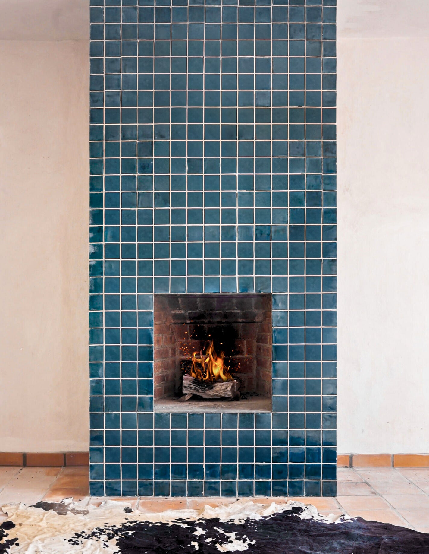 Deep teal blue Rio 4.25x4.25 solid tile by Clay Imports, forming a fireplace facade with a burning fire.