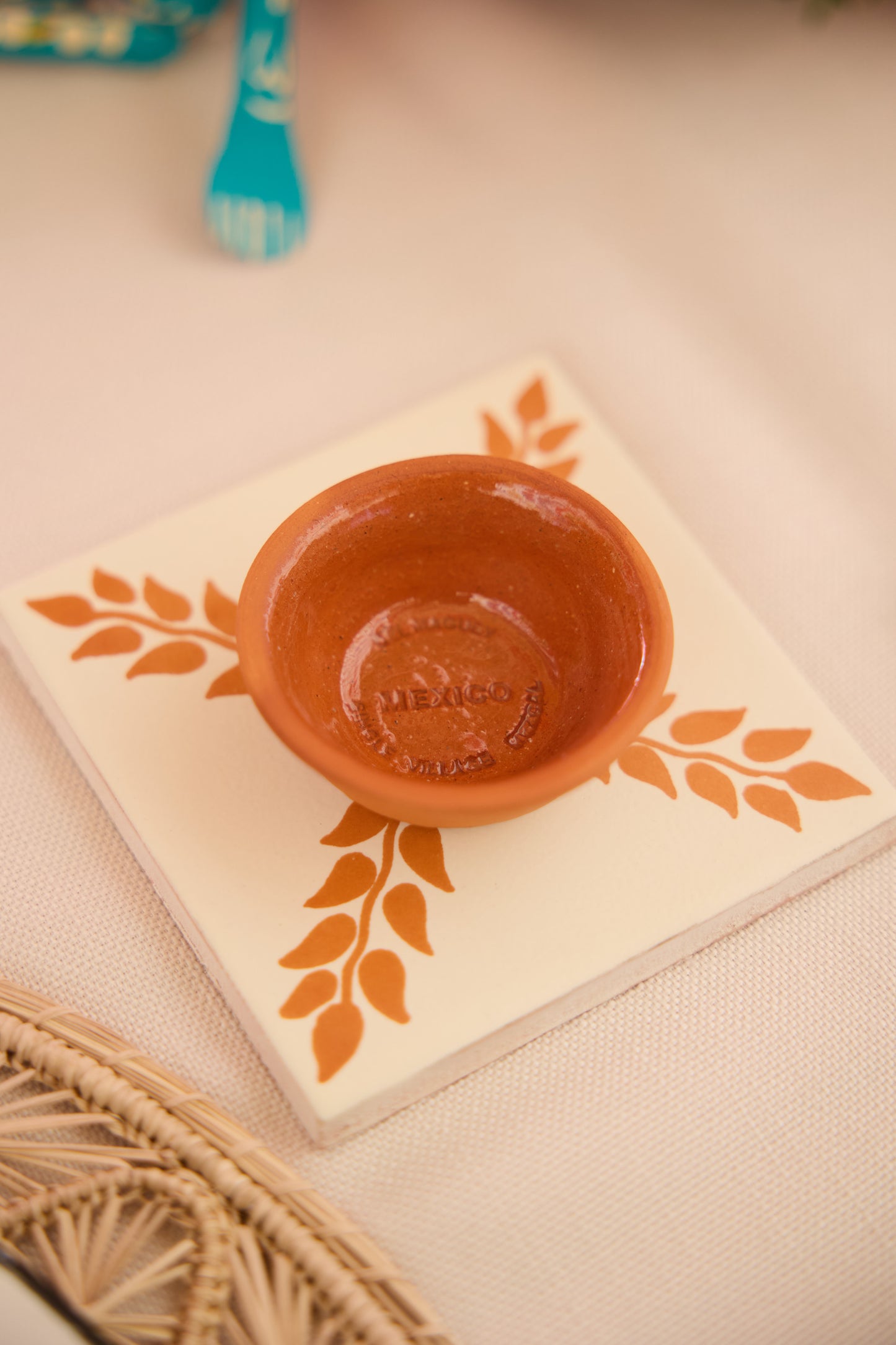 Square 4.25x4.25 cream Talavera tile by Clay Imports Handmade Tile, featuring an orange leaf pattern and a small terracotta bowl stamped 'MEXICO'.