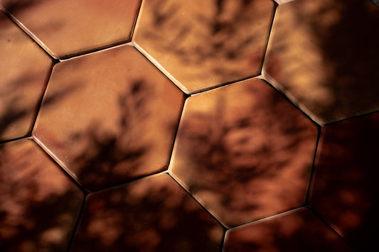 Sunlit hexagonal Saltillo tiles showcasing their natural warmth and texture under shifting leaf shadows.