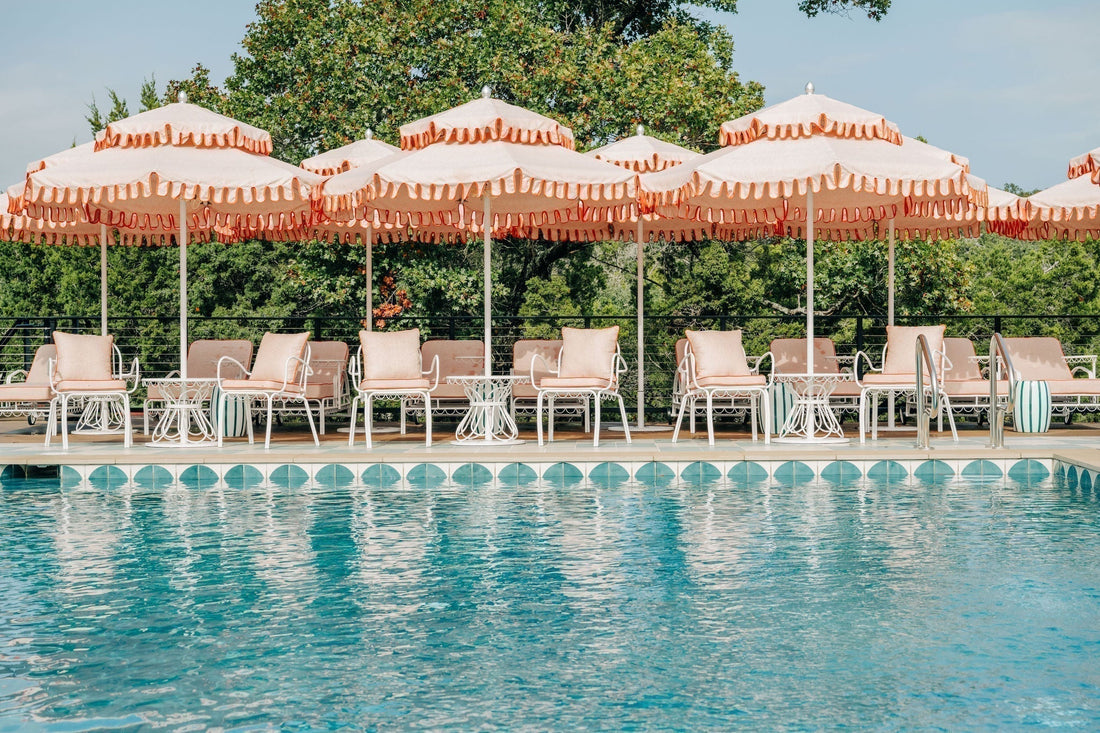A luxurious poolside scene with pink scalloped umbrellas, white lounge chairs, and unique blue patterned tiles at Camp Lucy's spa.