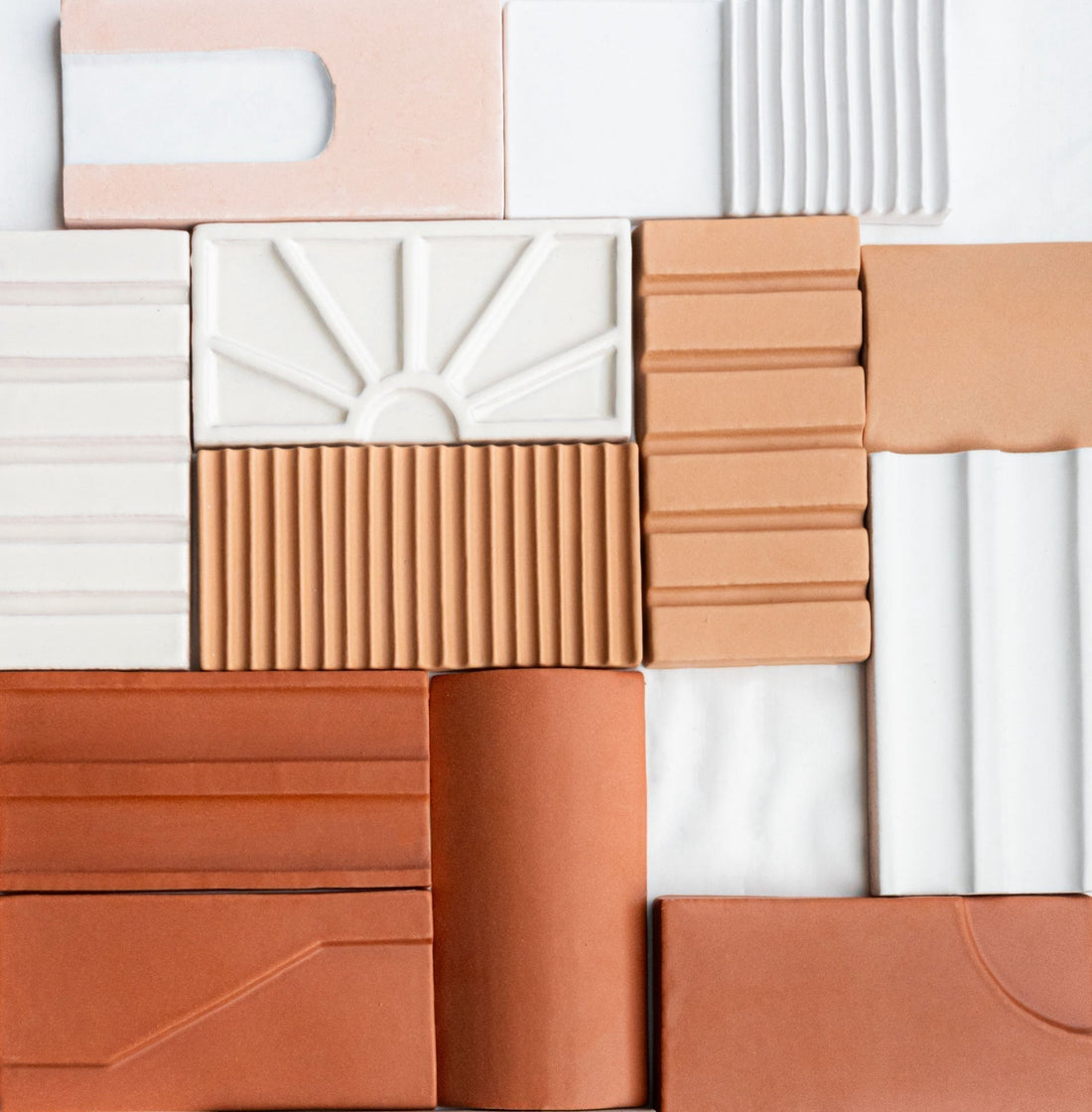 A flat lay of diverse modern tiles in peach, terracotta, and white, highlighting unique patterns and textures from the collaboration.