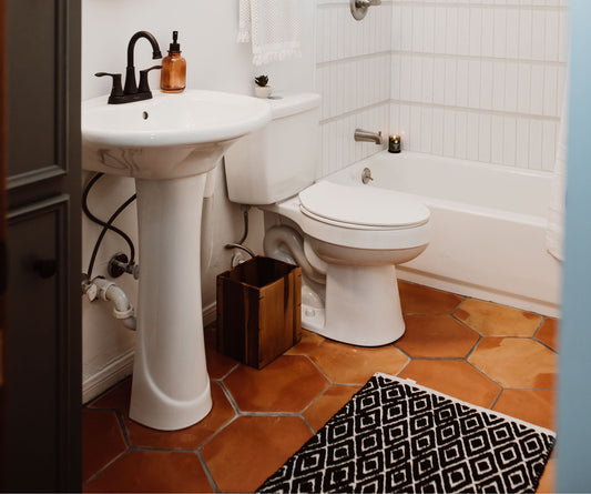 A beautifully renovated modern country bathroom featuring warm Saltillo hexagon tile floors and crisp white fixtures.