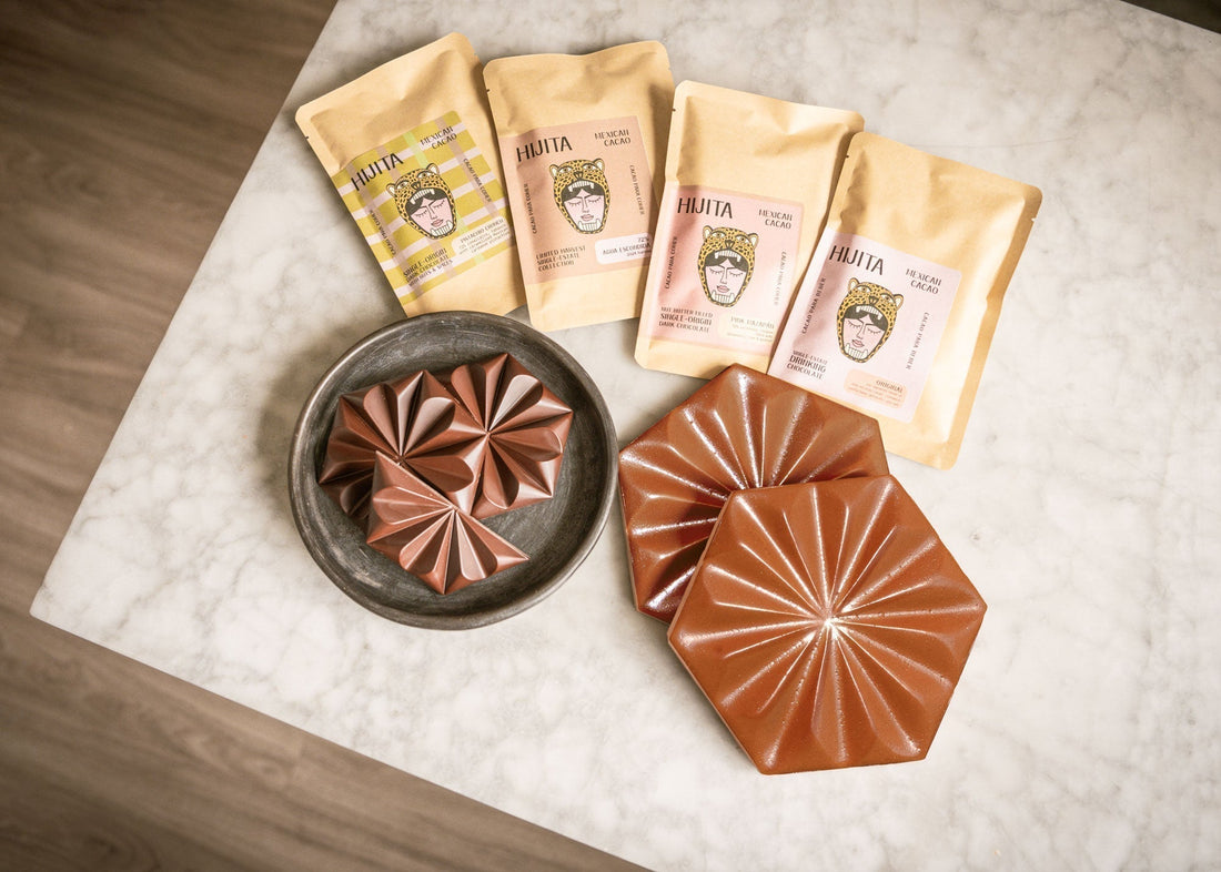 Artfully arranged Hijita Mexican cacao products, chocolate pieces, and complementary chocolate-inspired hexagon tiles on a marble surface.