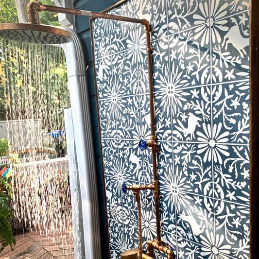 Refreshing DIY outdoor shower featuring exposed copper plumbing and whimsical blue and white patterned tiles.