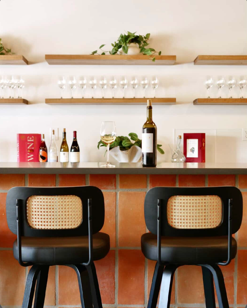 A modern wine bar showcases organic terracotta tiles on its base, paired with stylish black cane stools and wine displays.