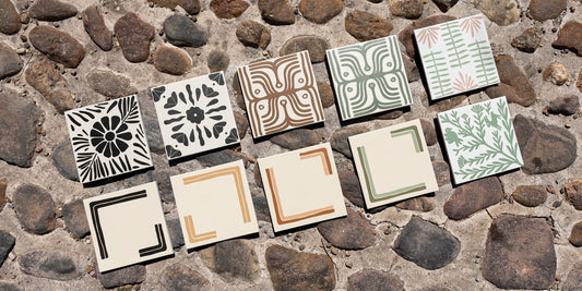 Diverse Otomi-inspired tiles with black, brown, and green patterns, featuring flora, fauna, and geometric designs, on a stone ground.