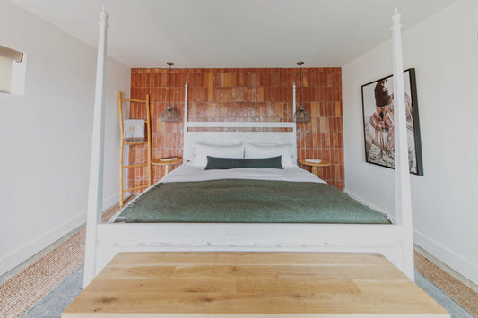 Cozy boutique hotel bedroom featuring a terracotta accent wall, white four-poster bed, and artwork reflecting Texas style.