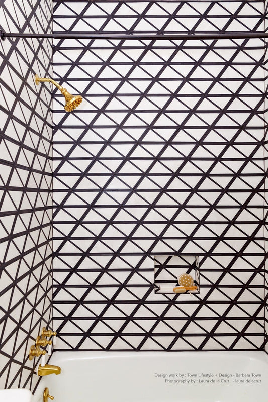 After remodel: Modern shower walls with bold black and white geometric triangle tiles and elegant gold fixtures.
