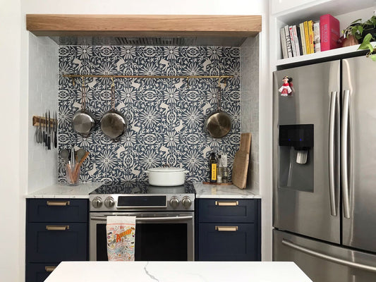 Denisse's dream kitchen features deep navy cabinets, brass hardware, and an exquisite blue and white patterned tile backsplash.