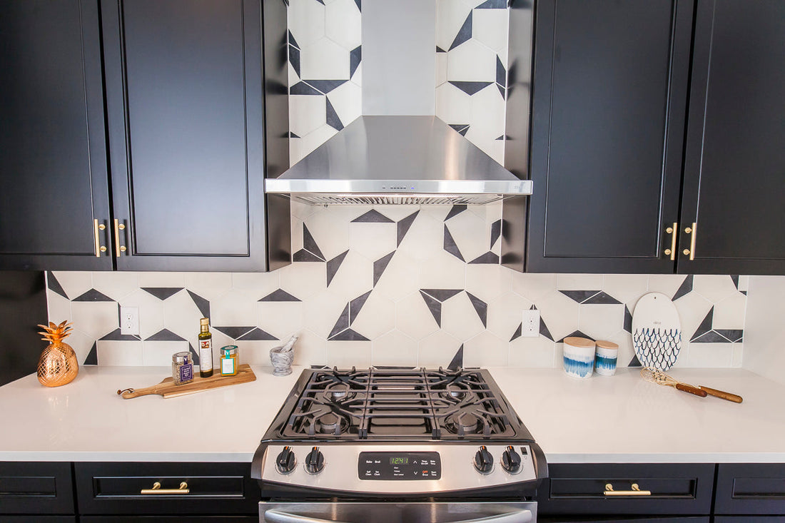 A modern kitchen showcases black cabinets, gold hardware, and a unique black and white geometric tile backsplash.