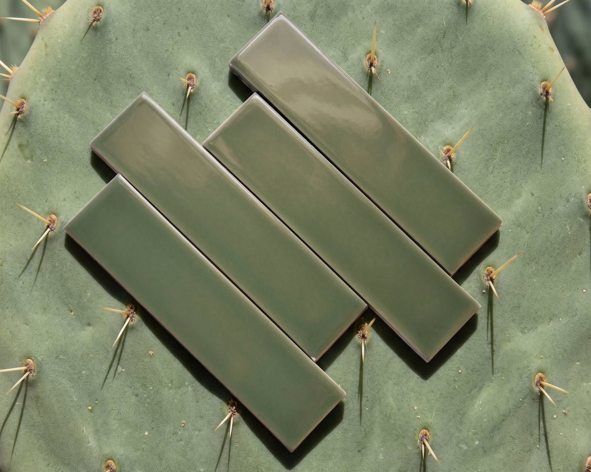 Glossy green 2x8 solid tile by Clay Imports, arranged diagonally on a light surface.