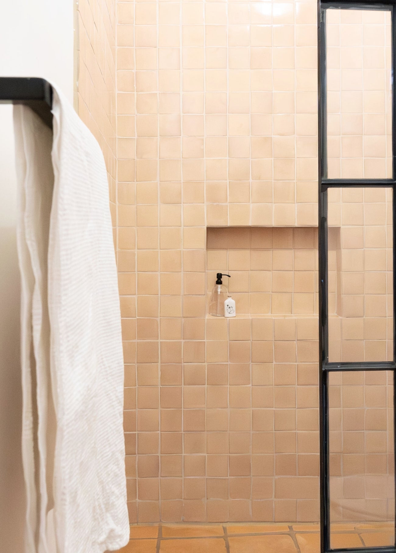 Apricot-toned tiled shower with a clear soap dispenser and white waffle towel, creating a warm, minimalist bath retreat.