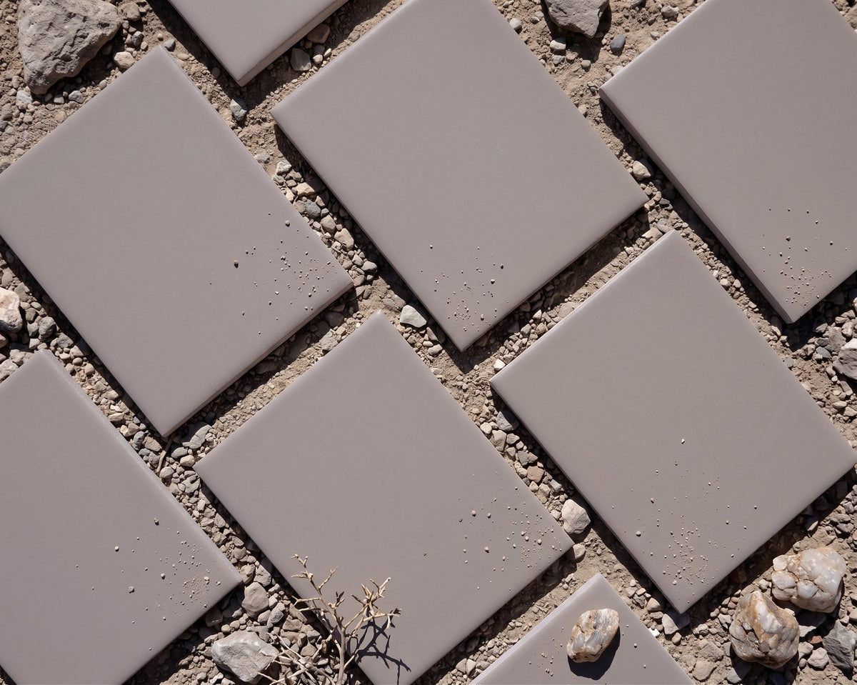 Matte grey solid tiles by Clay Imports, arranged diagonally on a light background, showing subtle texture and varying shadows.