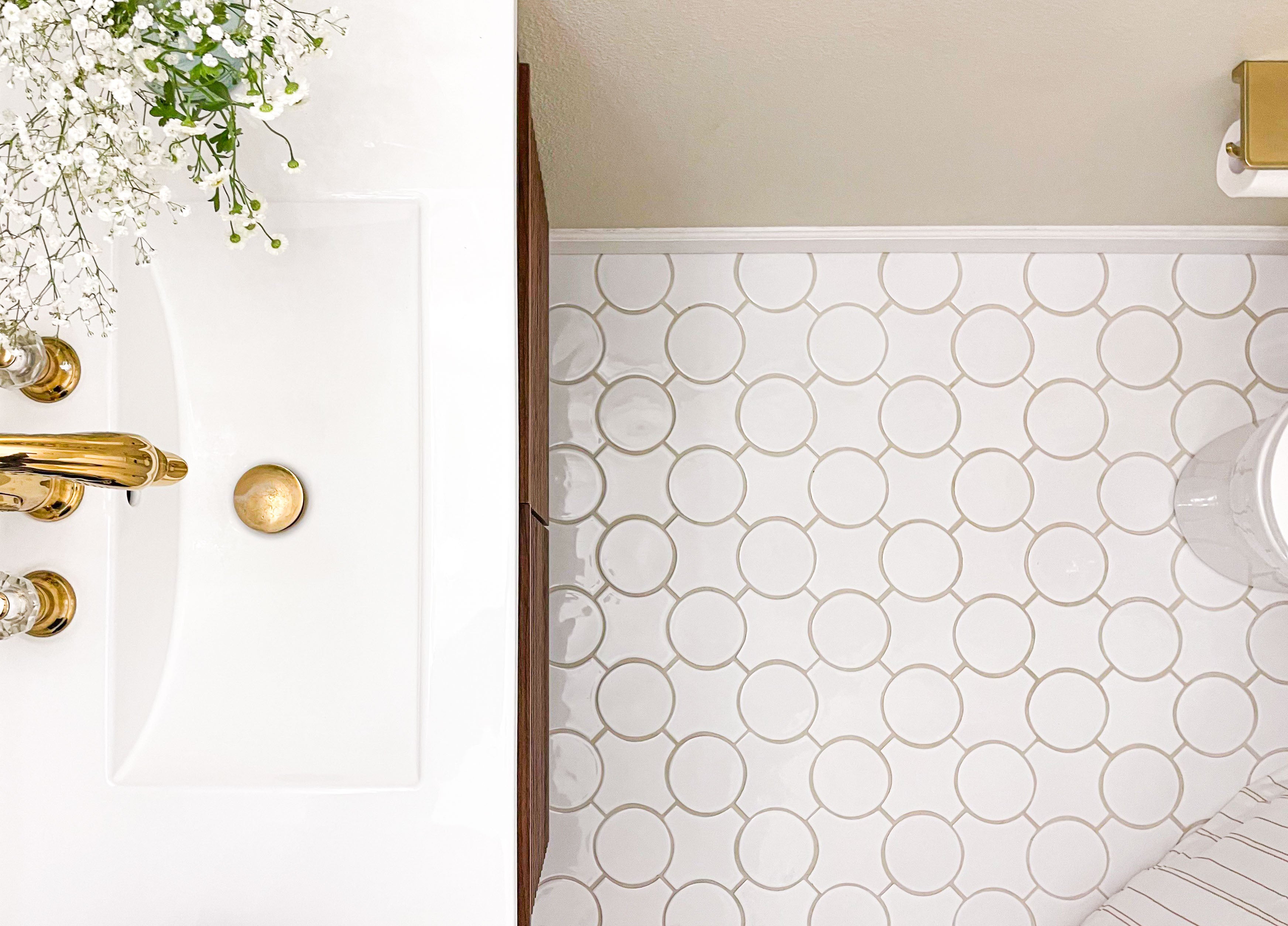 Luxurious bathroom featuring polished gold fixtures, delicate white florals, and eye-catching circular mosaic tiles.