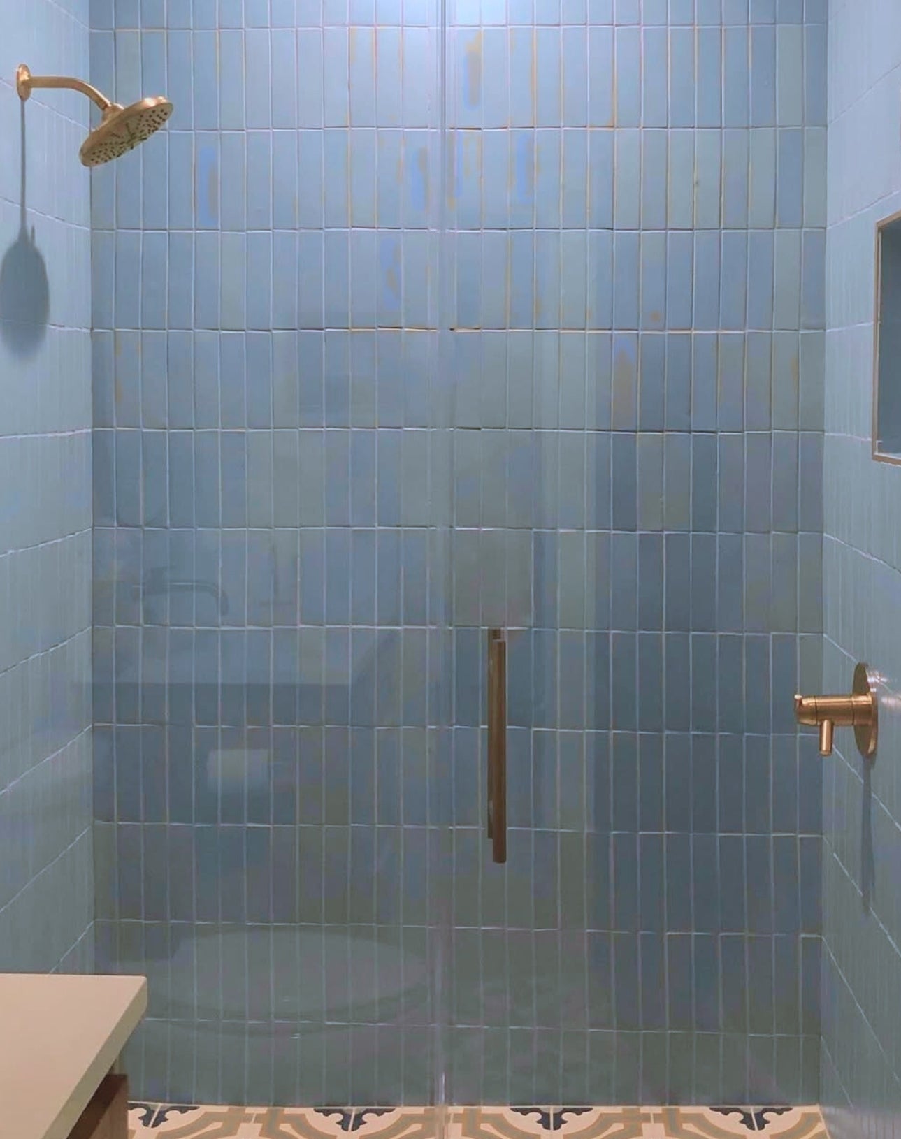 Serene shower featuring blue agate-inspired vertical tiles, gold fixtures, and elegant patterned floor.