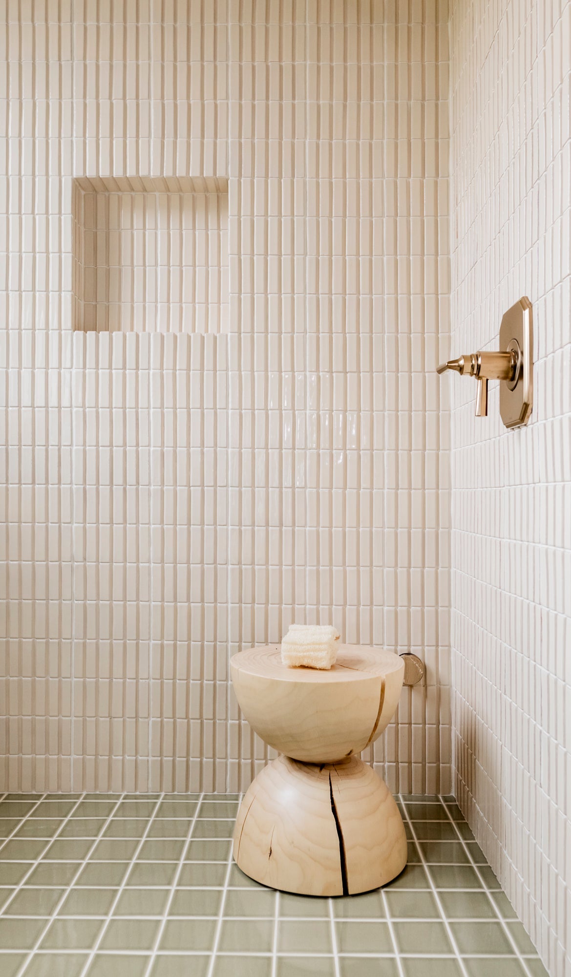 A serene shower with cream vertical picket tiles, natural wood stool, and sage green floor tiles, embodying modern organic tranquility.