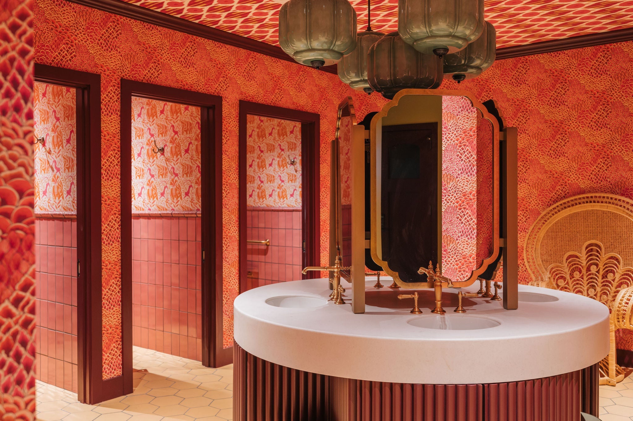 Vibrant, tropical-inspired bathroom featuring bold orange patterned wallpaper, elegant brass fixtures, and a unique vanity.