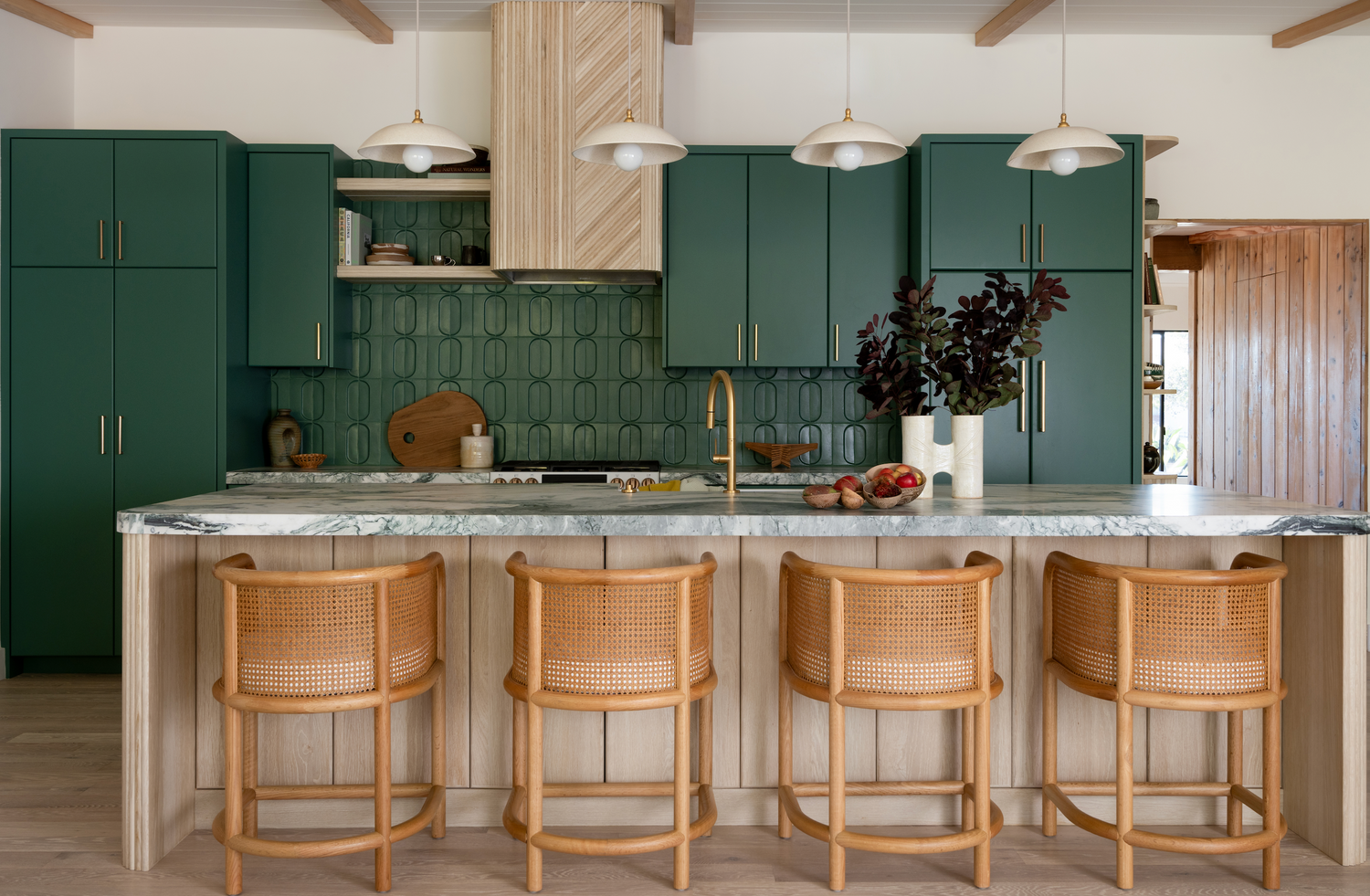 Modern kitchen with forest green cabinets, geometric tiles, wood accents, and rattan stools, showcasing refined home design.