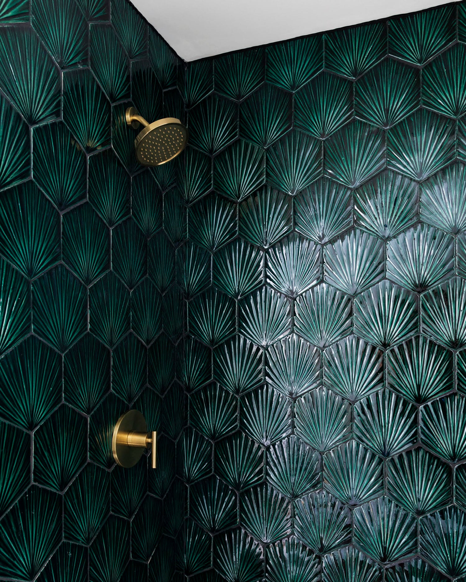 The Valladolid collection features bold emerald green fan-patterned hexagonal tiles and sleek brass bathroom fixtures, creating a lavish Art Deco look.