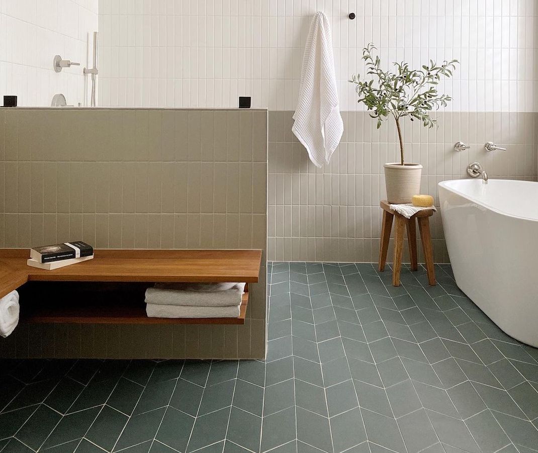 Elegant modern bathroom with vertically stacked white and green tiles, featuring a deep teal chevron floor and natural wood elements.