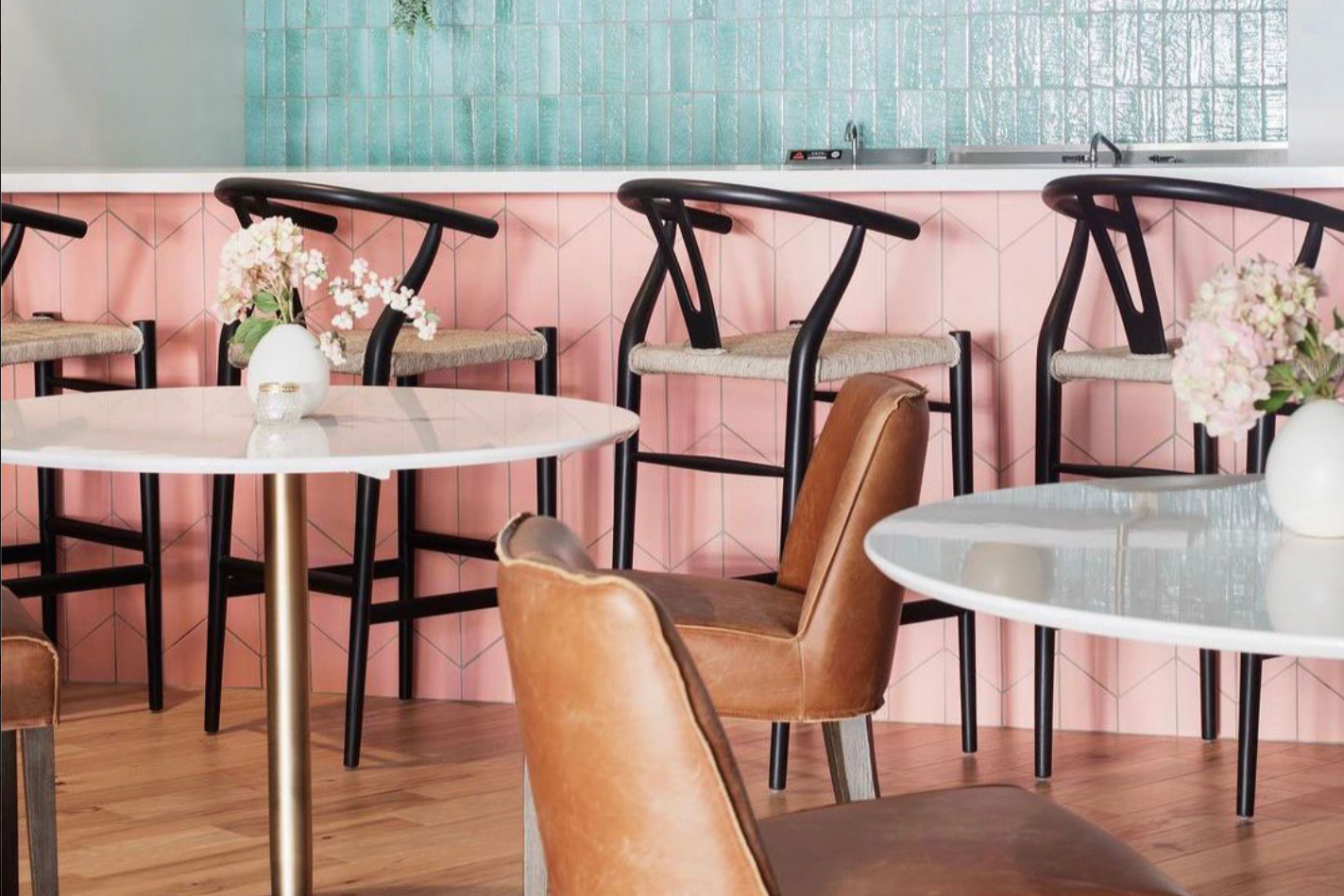 Chic cafe interior with pink herringbone tiles, modern seating, and fresh florals, embodying a vibrant, refreshing aesthetic.