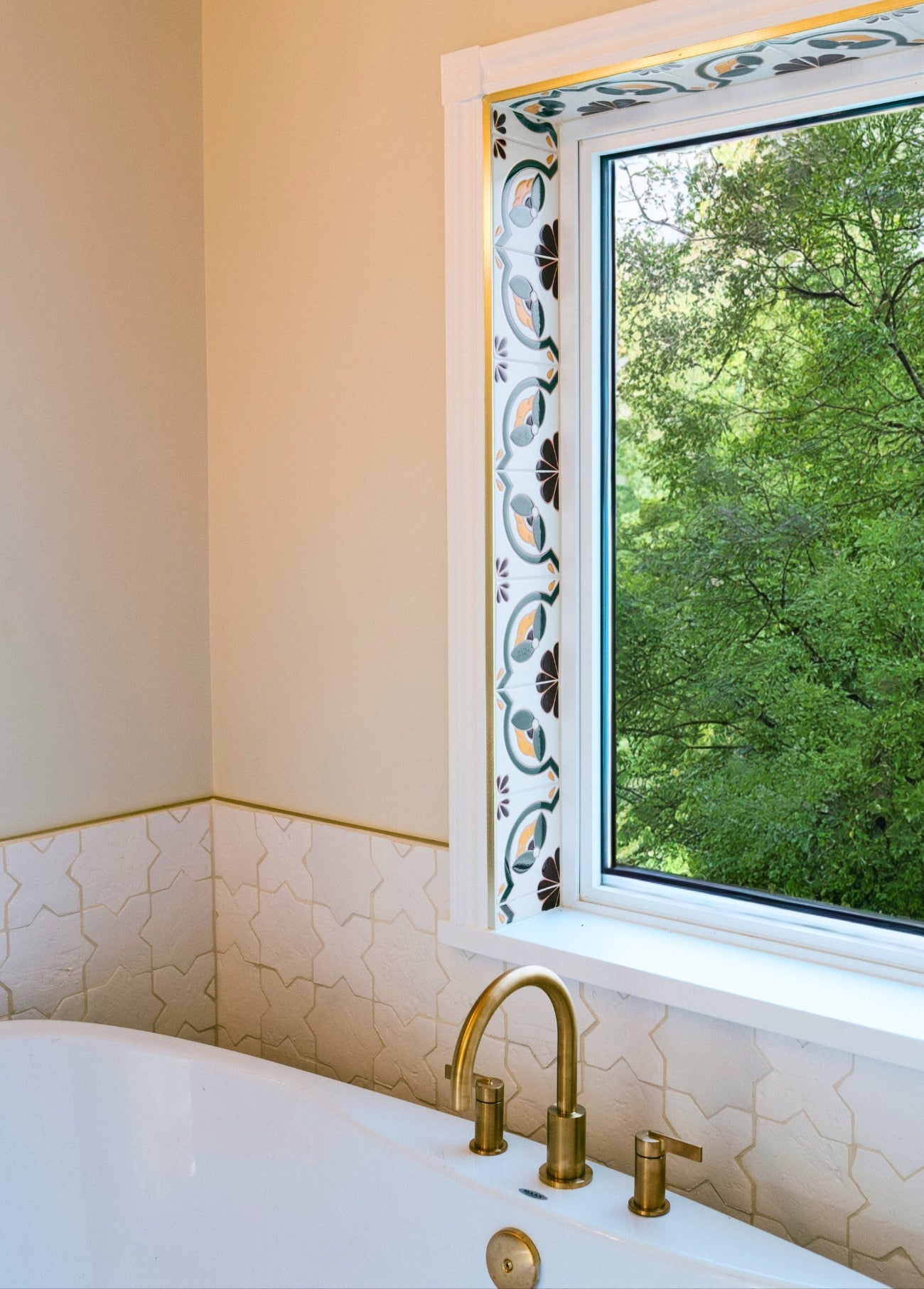 Artisanal handpainted relief tiles with intricate patterns beautifully frame a window, creating an elegant and serene bathroom space.