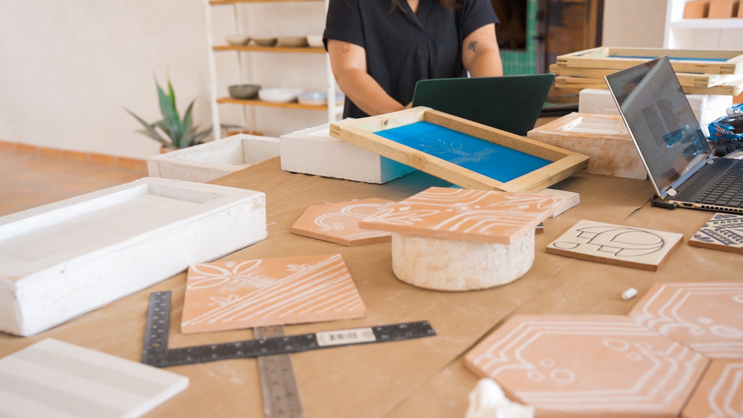 Handcrafted clay tiles featuring unique white designs, showcased in an artisan's studio with screen printing tools.