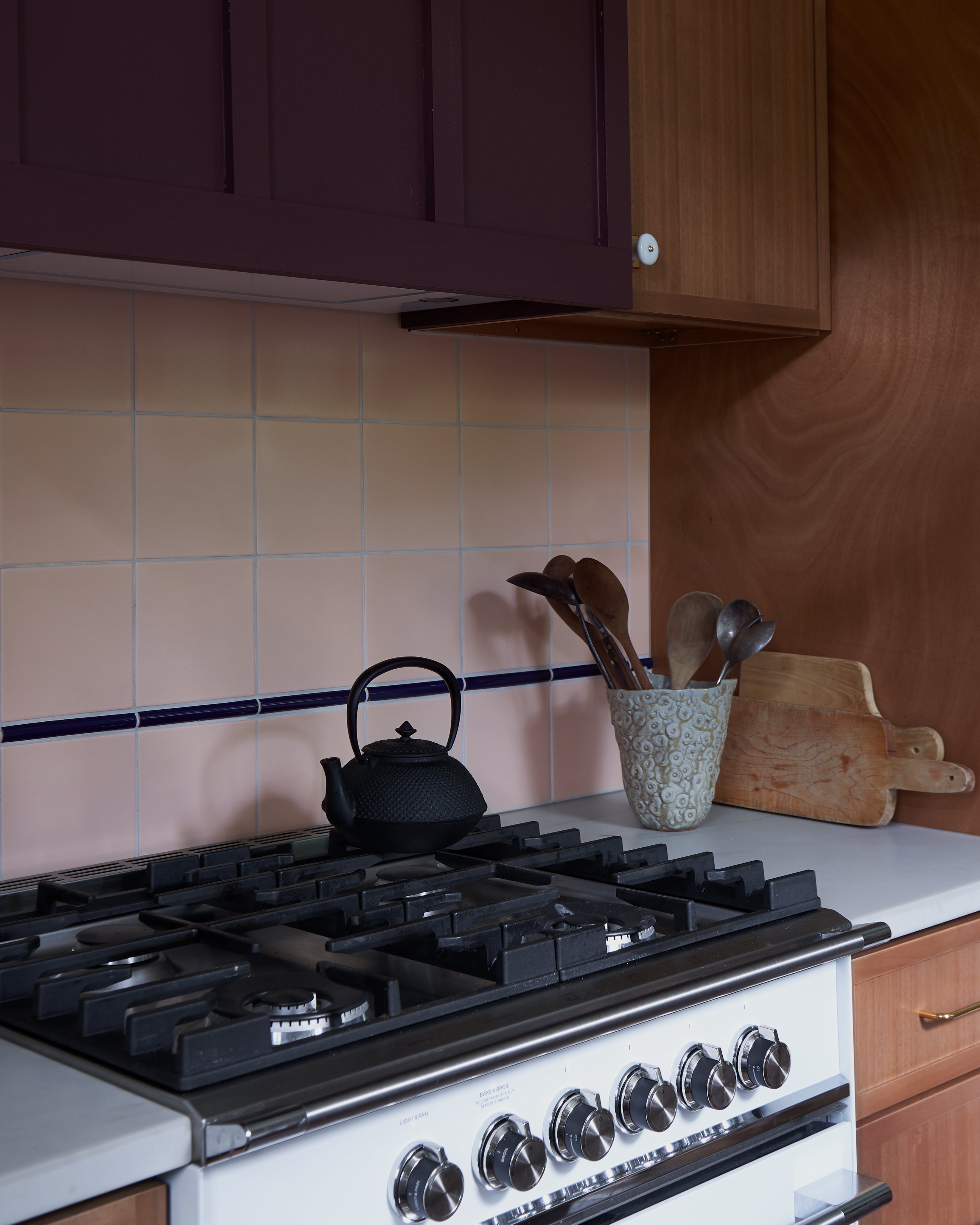 Desert-toned kitchen featuring peach tiles, warm wood, and contrasting dark cabinetry, accented with rustic cookware and a modern range.
