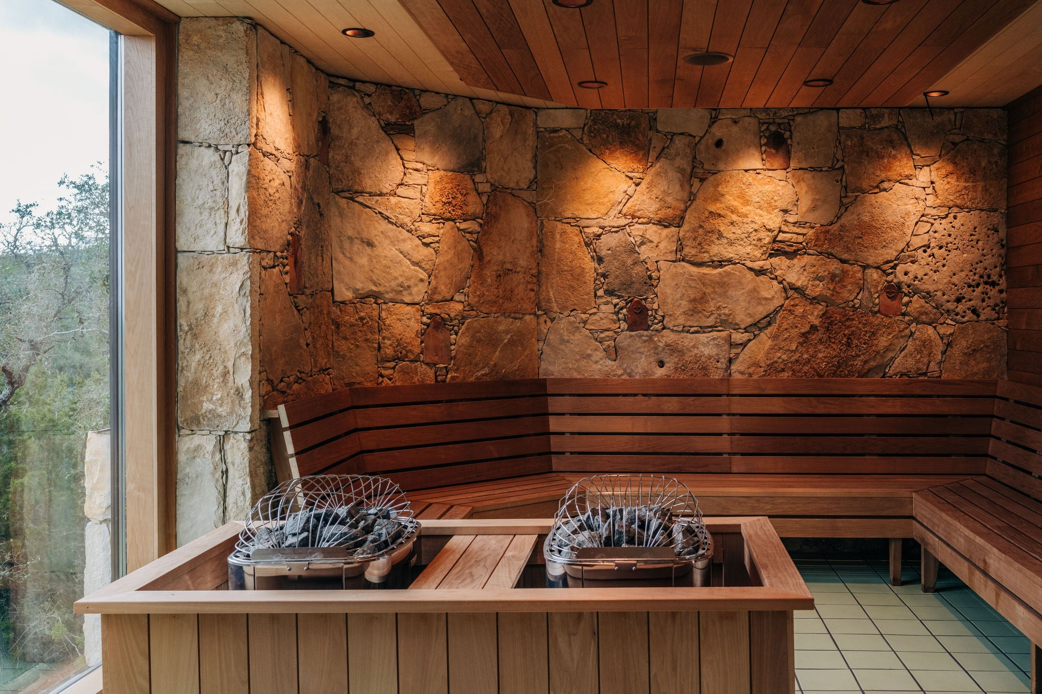 Serene sauna room featuring earthy stone walls, warm wood accents, and modern rock heaters for a luxurious natural wellness retreat.