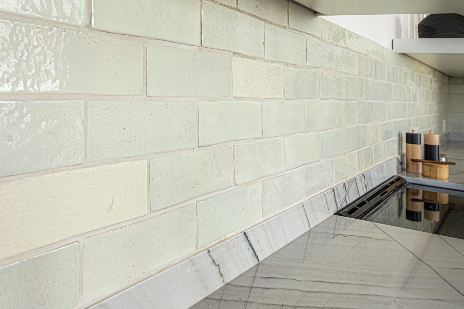 Fresh kitchen featuring artisanal pale green subway tiles with a textured finish and elegant natural stone countertops.