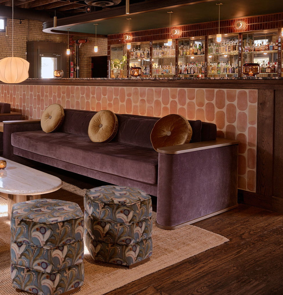 Modern lounge featuring a deep purple velvet sofa, patterned ottomans, and a tiled wall, exuding sophisticated comfort.