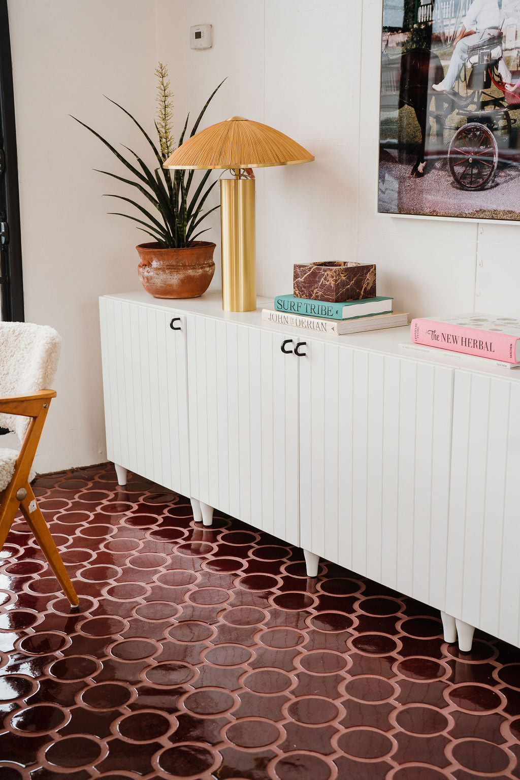 Glossy terracotta floor tiles with interconnected oval patterns reflect elegant mid-century wooden furniture.