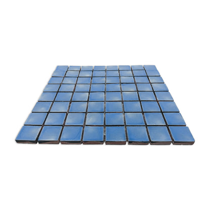 Blue meshed clay mosaic tile sheet by Clay Imports, featuring small squares with uneven surfaces and unglazed terracotta sides.