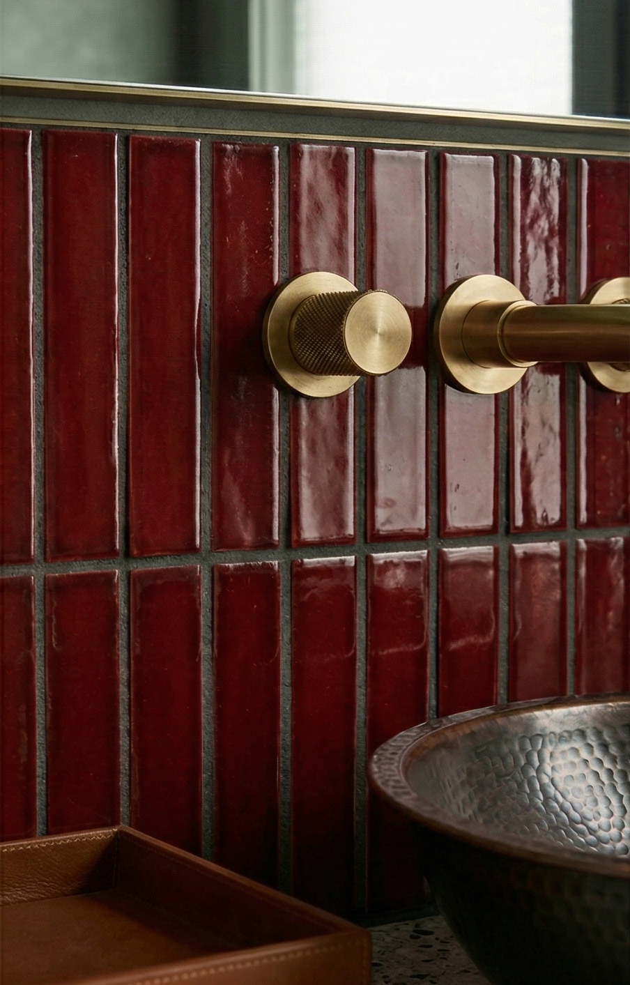 Oxblood solid tile by Clay Imports, rectangular matchstick tiles with dark grout, brass faucet, and hammered metal sink.