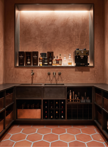 A luxury home bar setup featuring a copper-toned textured backlit wall, dark wood L-shaped cabinetry with integrated wine racks, a double sink with three chrome faucets, and a built-in shelf displaying various premium liquor bottles and bar equipment.