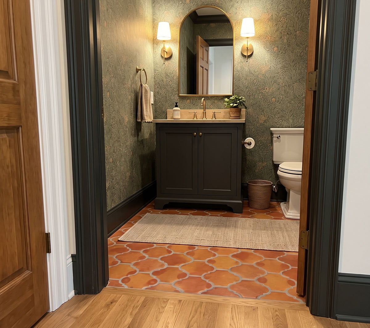A styled bathroom interior with a dark wood vanity, terracotta tile floor, textured green wallpaper, and a white toilet visible in the background, framed by dark wood door trim.