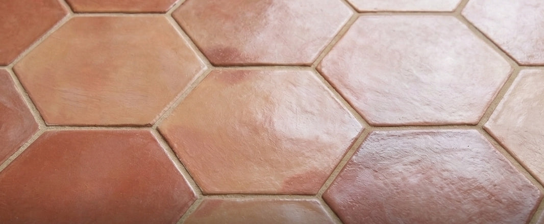 Terracotta rounded hexagon tiles by Clay Imports in varying earthy red tones, laid in a close-up, slightly uneven textured pattern.