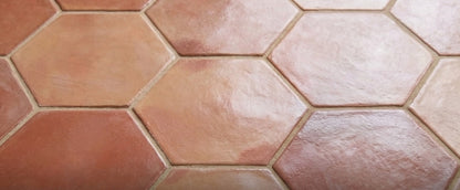 Terracotta rounded hexagon tiles by Clay Imports in varying earthy red tones, laid in a close-up, slightly uneven textured pattern.