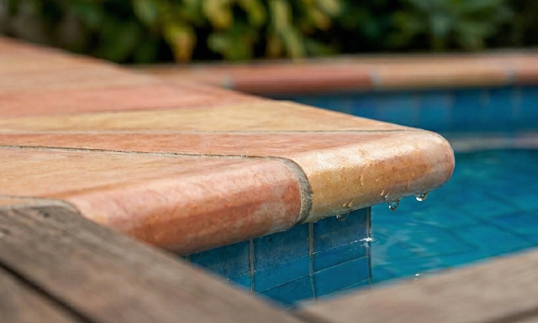 Smooth glossy terracotta coping by Clay Imports with water droplets on a rounded edge above blue pool tiles.