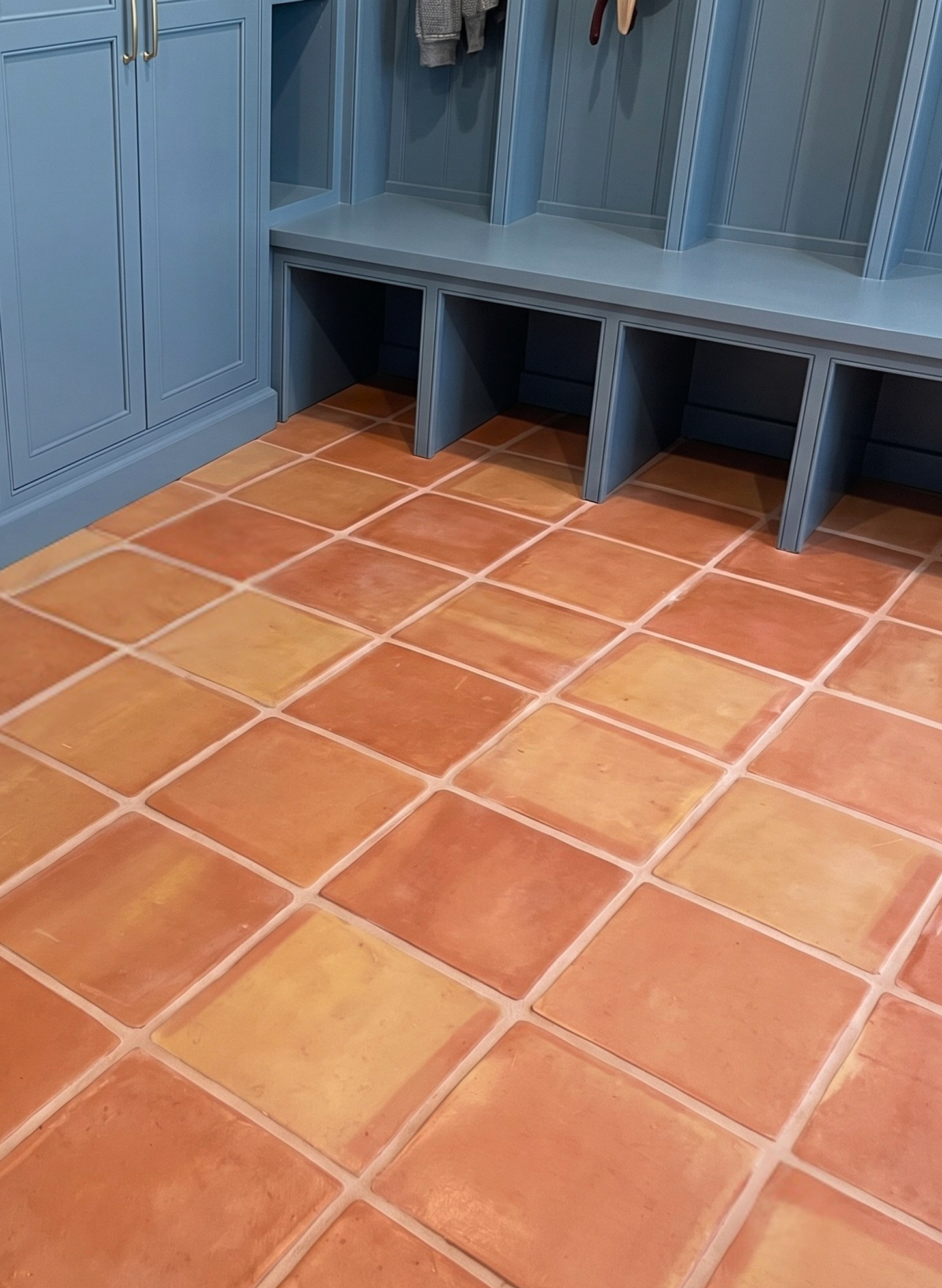 Terracotta square floor tiles with light grout lines, shown in a matching blue storage closet with shelves and cubbies.